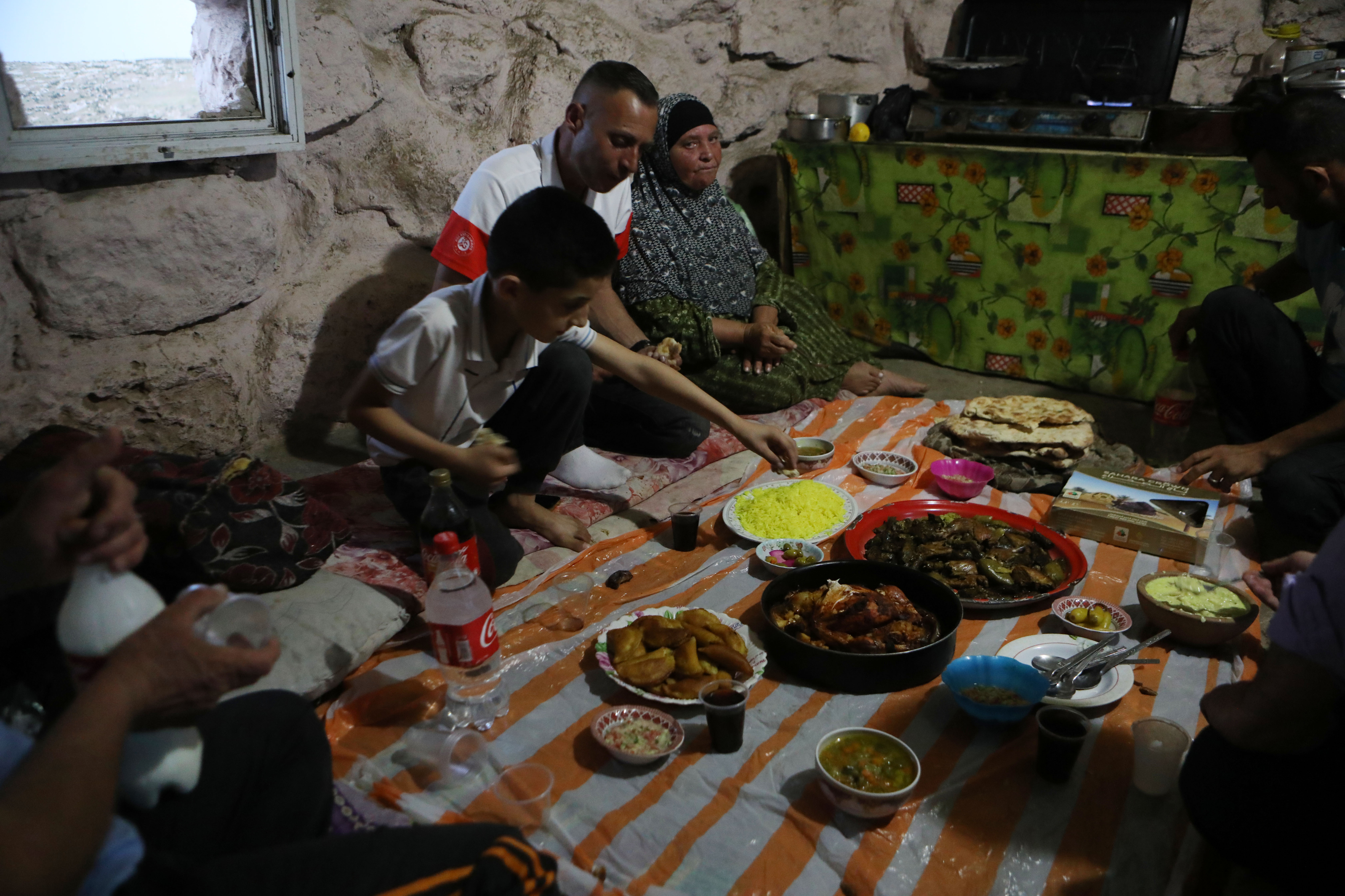عائلة فلسطينية تتناول إفطار طعام رمضان داخل كهف في قرية خربة زنوتا جنوب الخليل .. تصوير: شينخوا